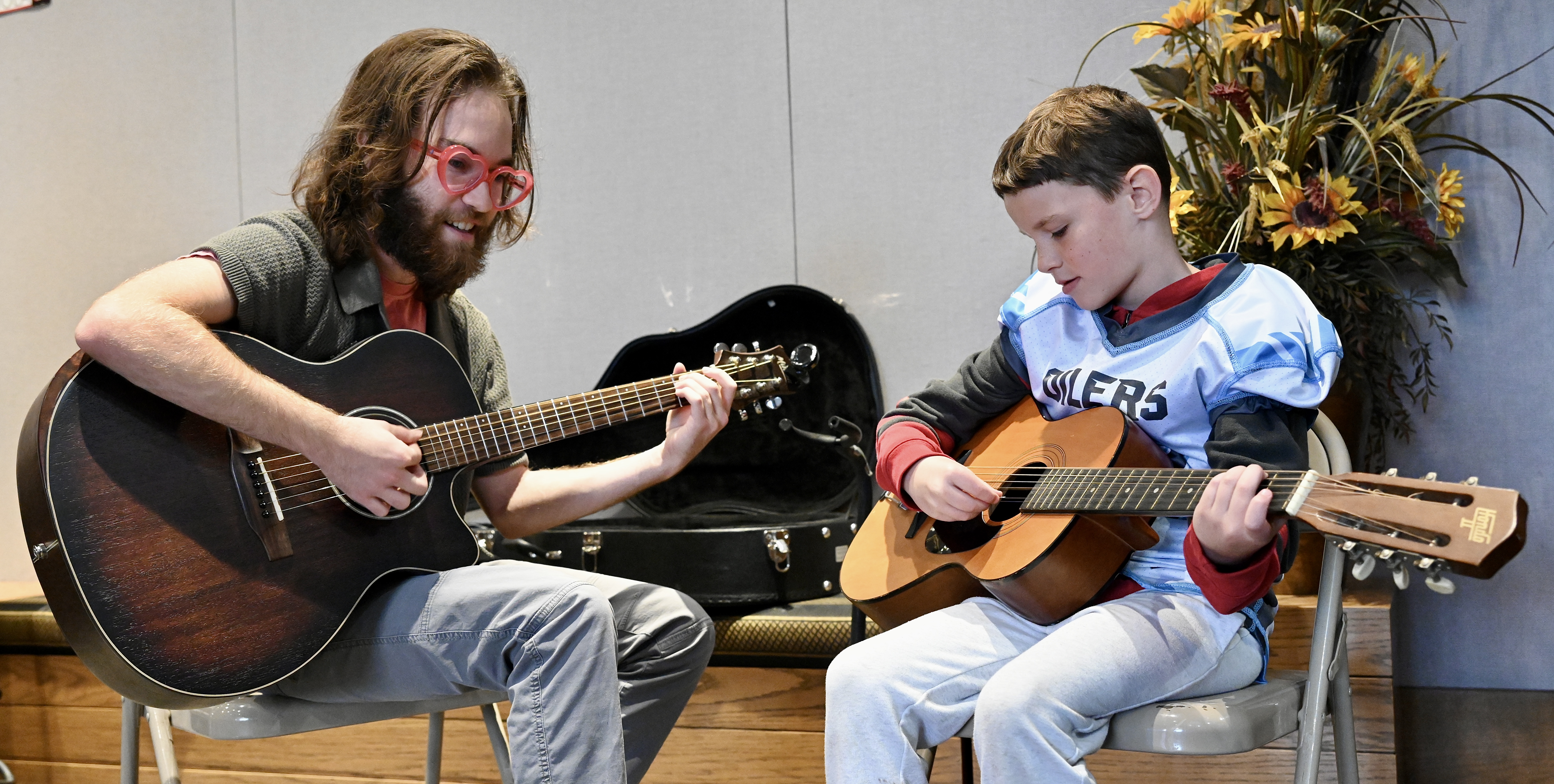 FHSU Music Education student smiles while teaching a young child how to play guitar.