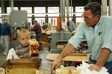 In this 2006 photo at the Teaming Up for Tots event at Fort Hays State University, Dr. Fred Ruda gets help from his grandson, 5-year-old Keith Millershaski, in dipping the front-end loaders into a container of Danish oil.
